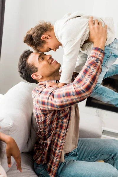 Abgeschnittene Ansicht einer Frau, die in der Nähe eines afrikanisch-amerikanischen Vaters sitzt, während ein Mann ein Kind in der Luft hält — Stockfoto