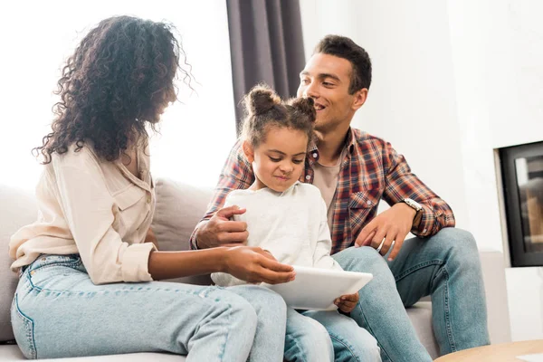 Criança brincando com tablet digital enquanto os pais afro-americanos sorrindo e olhando um para o outro — Fotografia de Stock