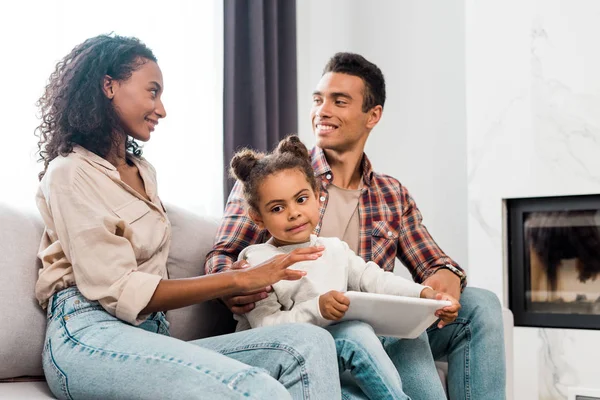Kid holding digital tablet while african american parents looking at each other — Stock Photo