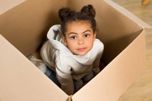 Vista de ángulo alto de niño lindo sentado en la caja y mirando a la cámara - foto de stock