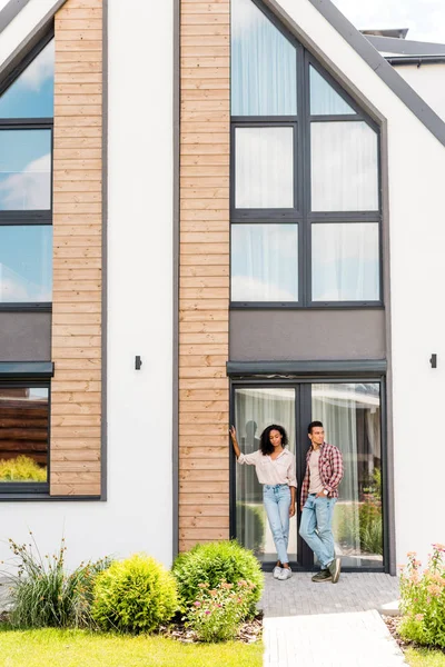 Full length view of african american man and woman standing outside near house — Stock Photo