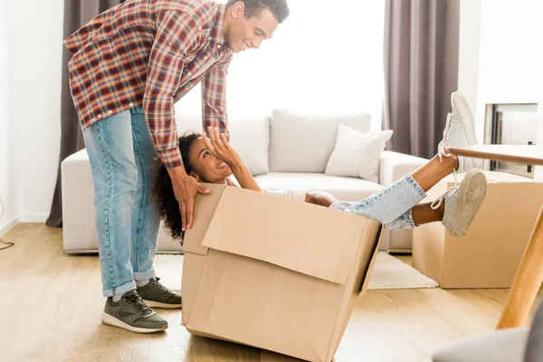 Full length view of african american man and woman looking at each other while husband trying to move box with wife — Stock Photo