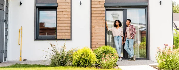 Panoramic shot of african american man and woman standing outside near house — Stock Photo