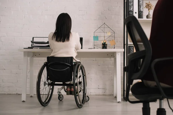 Vista posteriore della donna d'affari disabile seduta sul posto di lavoro in sedia a rotelle — Foto stock