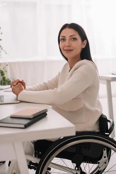 Веселая предпринимательница-инвалид смотрит в камеру, сидя на рабочем месте — стоковое фото