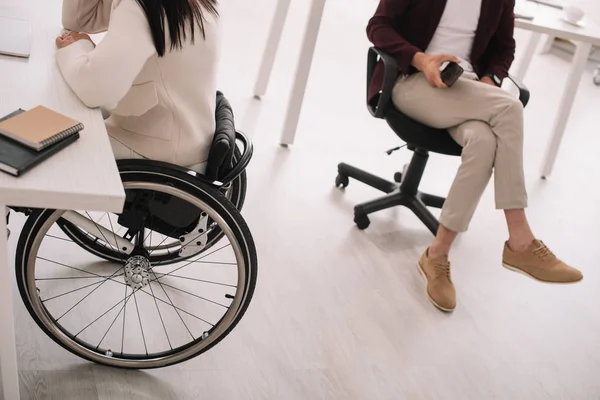 Vista recortada de la mujer de negocios en silla de ruedas cerca de socio de negocios en la oficina — Stock Photo