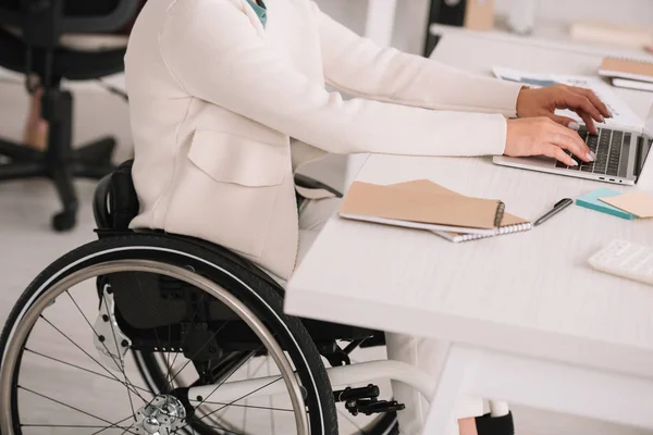 Vista recortada de la mujer de negocios discapacitada escribiendo en el ordenador portátil mientras está sentado en el lugar de trabajo - foto de stock