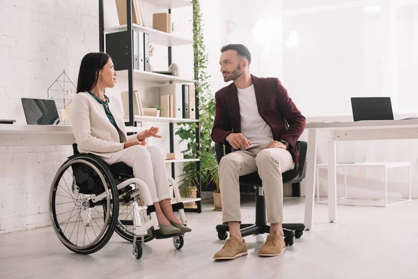 Disabled businesswoman in wheelchair gesturing while talking to business partner in office — Stock Photo