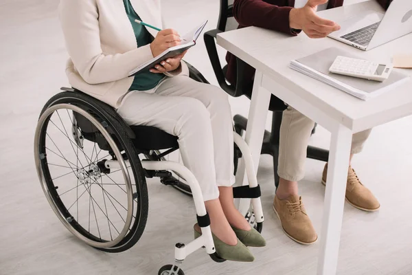 Обрізаний вид інвалідів бізнес-леді, що пише в блокноті, сидячи в інвалідному візку біля коледжу — стокове фото
