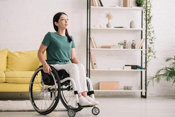 Усміхнена жінка з обмеженими можливостями дивиться в сторону, сидячи в інвалідному візку вдома — стокове фото