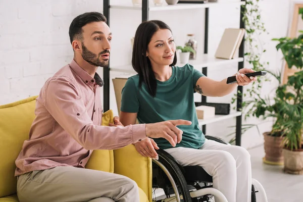 Handsome man pointing with finger while watching tv together with disabled girlfriend — Stock Photo