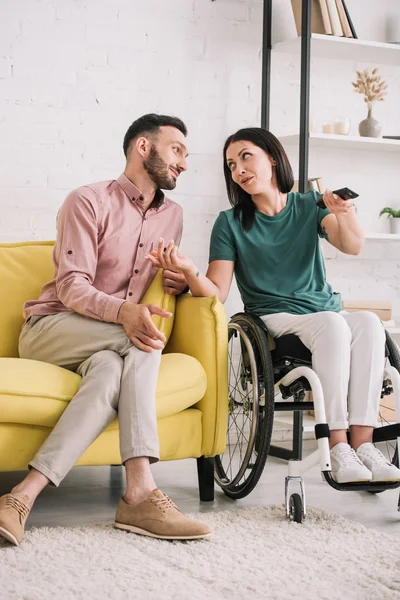 Mulher deficiente atraente conversando com namorado bonito enquanto assiste tv juntos em casa — Fotografia de Stock