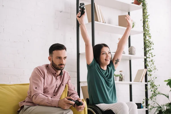 KYIV, UKRAINE - JULY 10, 2019: Happy disabled woman showing yes gesture while playing video game with boyfriend at home. — Stock Photo