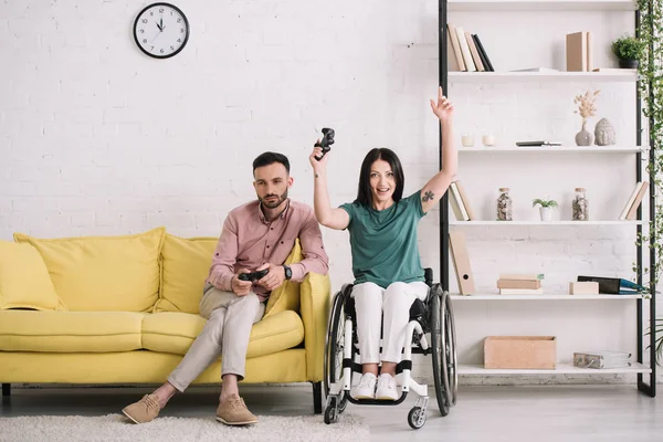 KYIV, UKRAINE - JULY 10, 2019: Excited disabled woman showing yes gesture while playing video game with boyfriend at home. — Stock Photo