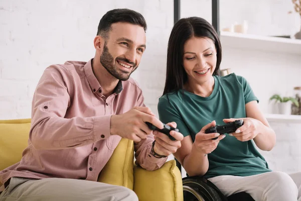 KYIV, UCRANIA - 10 de julio de 2019: Hombre alegre con novia discapacitada jugando videojuegos en casa . - foto de stock