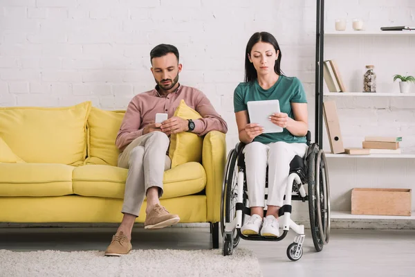 Внимательная женщина-инвалид с цифровым планшетом рядом красивый парень сидит на диване со смартфоном — стоковое фото