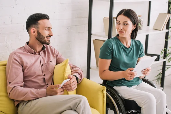 Mujer discapacitada feliz usando tableta digital cerca de novio sentado en el sofá con teléfono inteligente - foto de stock