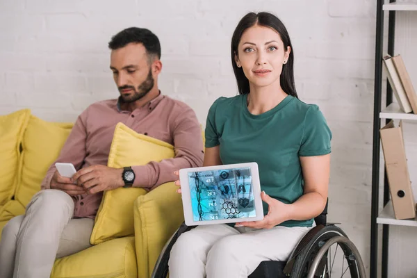 Young disabled woman showing digital tablet with dna information app while sitting near boyfriend using smartphone — Stock Photo