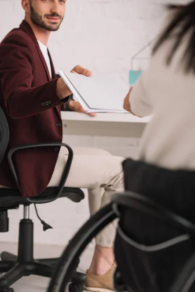 Vue recadrée du gestionnaire souriant donnant des documents à une femme d'affaires handicapée au bureau — Photo de stock