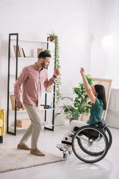 Young disabled woman on wheelchair dancing with handsome boyfriend at home — Stock Photo