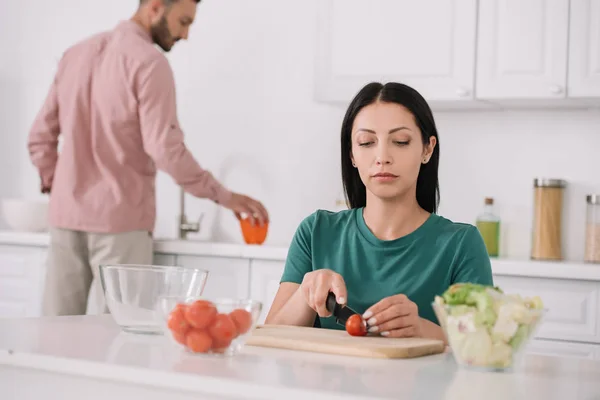 Enfoque selectivo de la mujer joven cortando tomate en la tabla de cortar - foto de stock