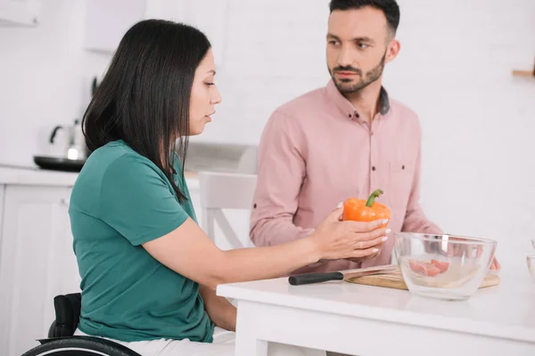 Jeune femme handicapée tenant poivron tout en parlant à petit ami dans la cuisine — Photo de stock