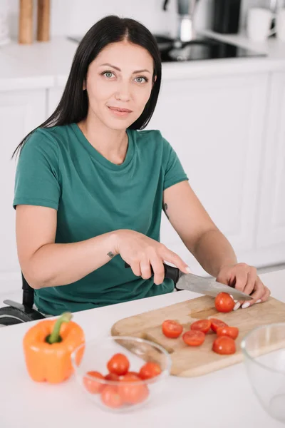 Schöne behinderte Frau schneidet Tomaten, während sie in die Kamera schaut — Stockfoto