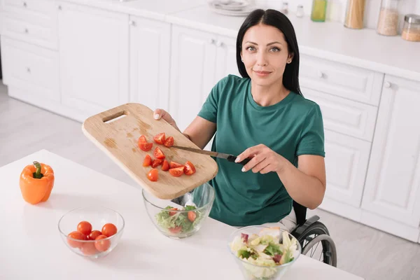 Alegre mujer discapacitada mirando a la cámara, mientras que la adición de tomates en rodajas en un tazón - foto de stock