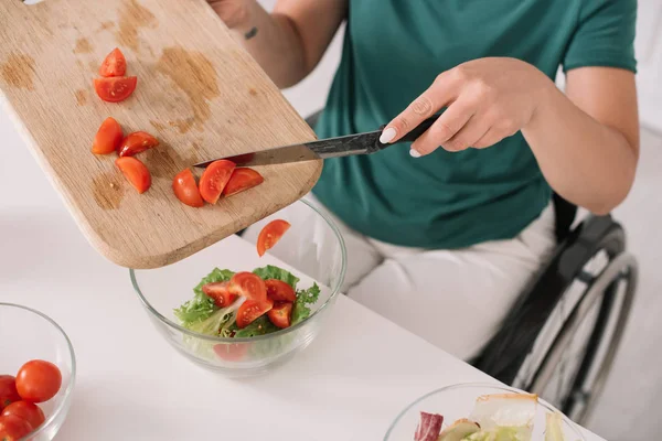 Vista parziale della donna disabile che aggiunge pomodori a fette in una ciotola di vetro in cucina — Foto stock