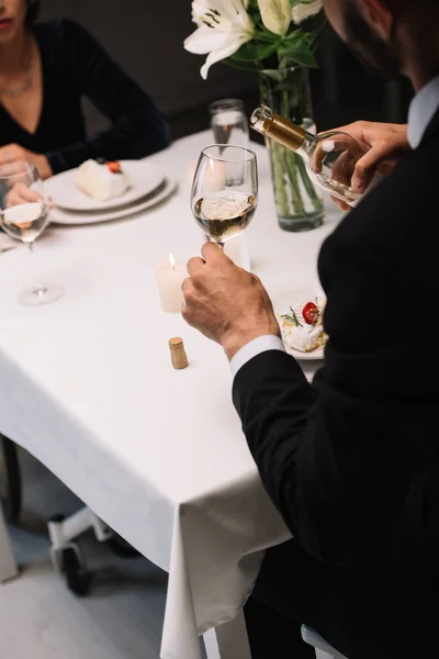 Cropped view of man pouring white wine in glass while having romantic dinner with disabled girlfriend — Stock Photo