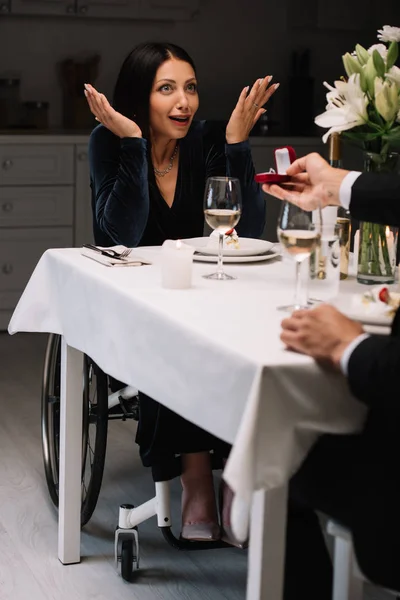 Vista recortada del hombre haciendo propuesta de boda feliz, sorprendida novia discapacitada durante la noche romántica - foto de stock