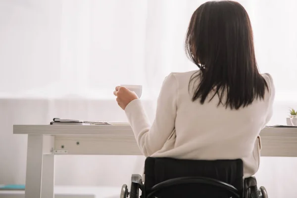 Vista posteriore della donna d'affari disabile seduta sul posto di lavoro in sedia a rotelle — Foto stock