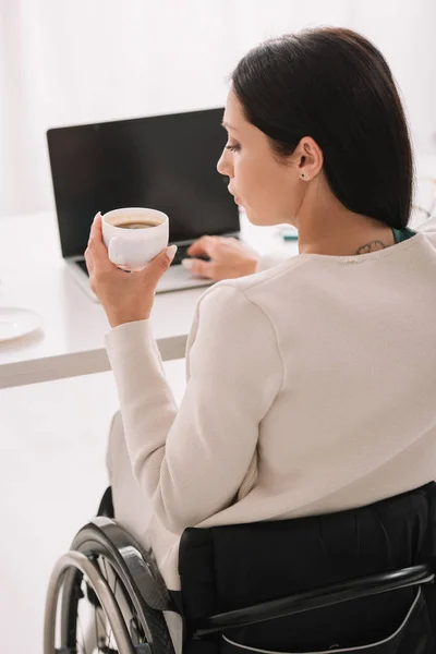 Вид ззаду бізнес-леді, що тримає чашку кави, використовуючи ноутбук в офісі — стокове фото
