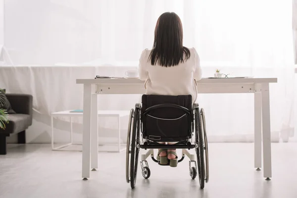 Visão traseira de empresária sentada em cadeira de rodas perto da mesa no escritório — Fotografia de Stock