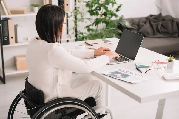 Joven mujer de negocios discapacitada utilizando el ordenador portátil mientras está sentado en silla de ruedas en el lugar de trabajo - foto de stock
