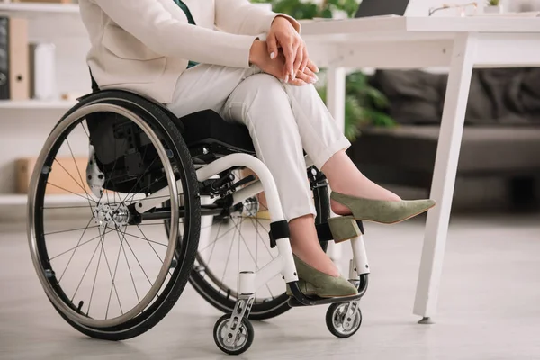 Vista recortada de la mujer de negocios discapacitada sentada en silla de ruedas con las piernas cruzadas - foto de stock