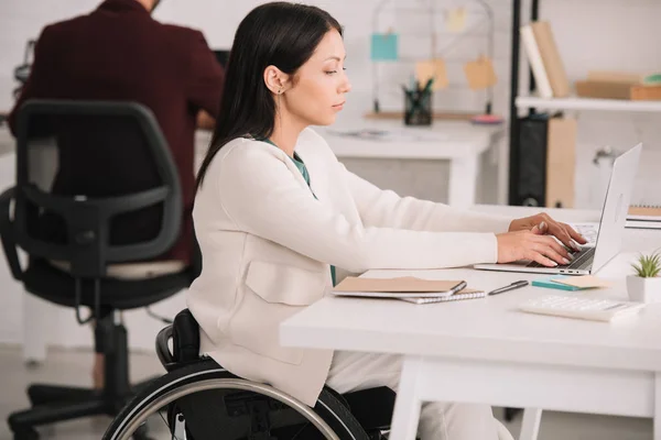 Donna d'affari disabile che digita sul computer portatile mentre siede sul posto di lavoro in offesa — Foto stock