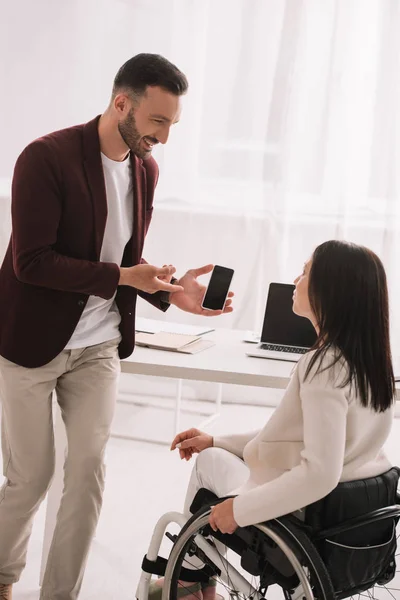 Gerente sorrindo mostrando smartphone com tela em branco para empresária com deficiência — Fotografia de Stock