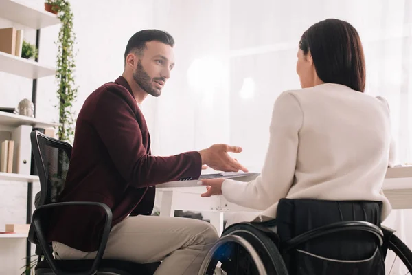 Hombre de negocios guapo y mujer de negocios discapacitada haciendo gestos mientras habla en el cargo - foto de stock