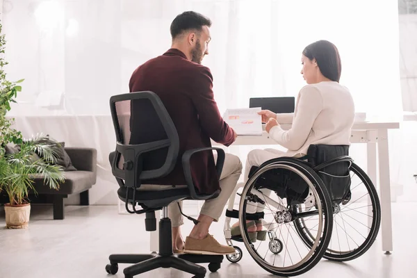 Disabled businesswoman in wheelchair showing documents to business partner in office — Stock Photo