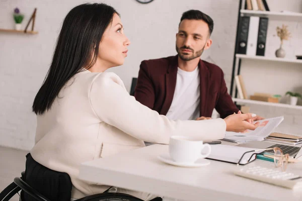 Serious businesswoman looking up and gesturing while sitting at desk near handsome colleague — Stock Photo