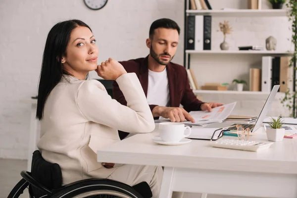 Attractive disabled businesswoman sitting at desk in office near handsome colleague — Stock Photo