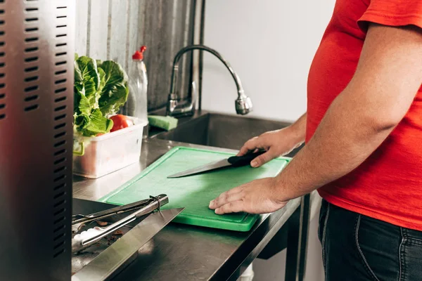 Vista parcial del cocinero con cuchillo y tabla de cortar en el lugar de trabajo - foto de stock