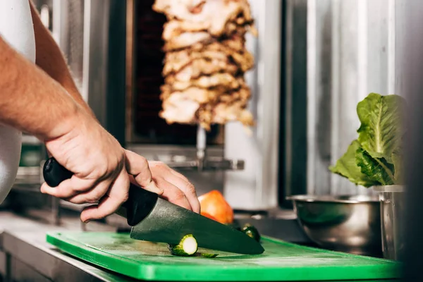 Cropped view of cook cutting cucumbers on chopping board — Stock Photo