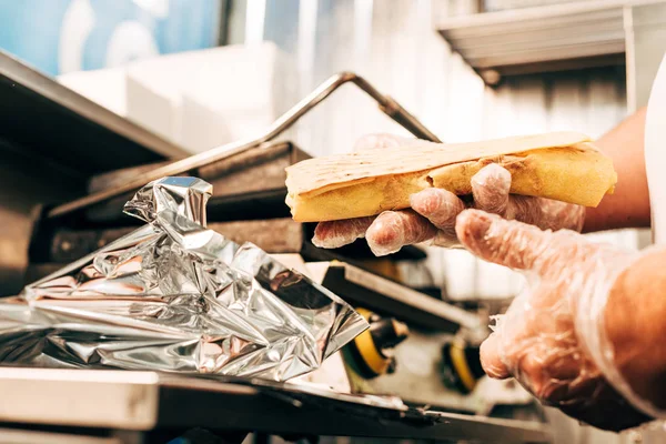 Partial view of cook in gloves using aluminium foil while preparing doner kebab — Stock Photo