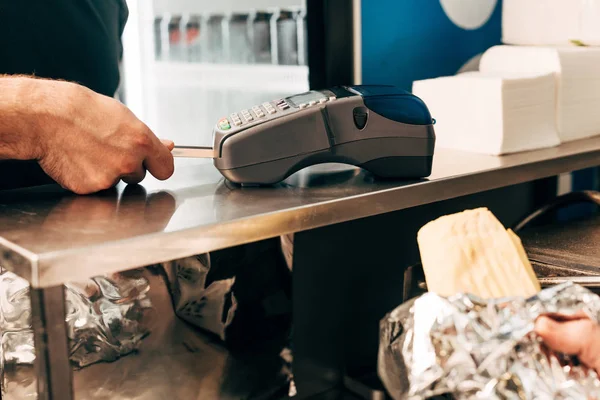 Cropped view of man buying doner kebab in aluminium foil and cashier using payment terminal — Stock Photo