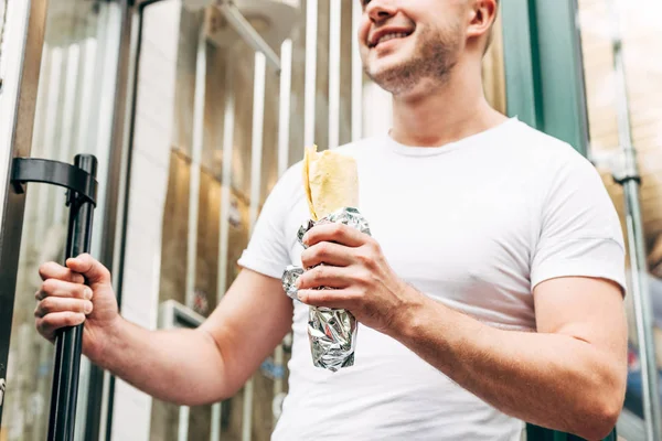 Partial view of smiling man holding doner kebab in aluminium foil — Stock Photo