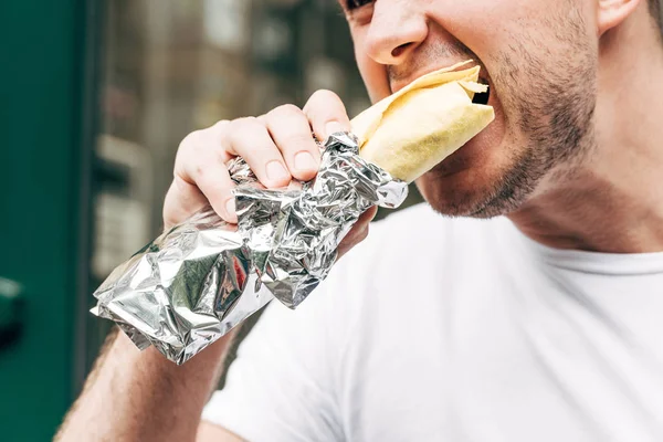 Cropped view of man eating doner kebab in aluminium foil — Stock Photo