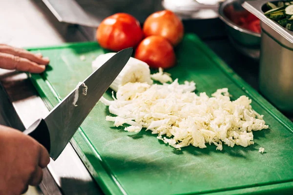 Cropped view of cook holding knife near cutting board with lettuce and tomatoes — Stock Photo