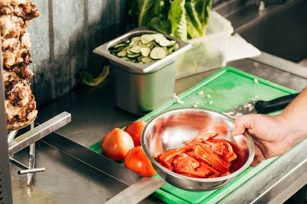 Обрезанный вид на повара, держащего миску с нарезанными помидорами — стоковое фото